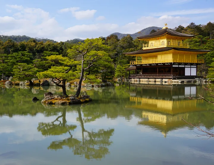 The Golden Pavilion of Kinkaku-ji reflected in still green water, framed by pines and a small rock island.